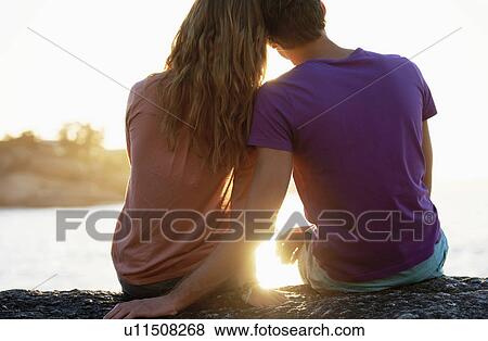 Rear view of young couple sitting at beach View Large Photo Image Stock Photo - Rear view of young couple sitting at beach. Fotosearch