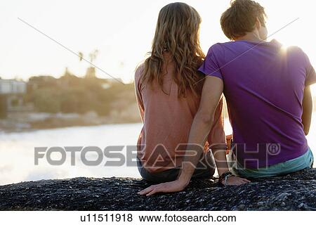 Rear view of young couple sitting at beach View Large Photo Image Stock Photo - Rear view of young couple sitting at beach. Fotosearch