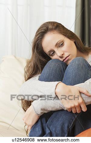 Stock Photo - Sad woman sitting on sofa and looking away. Fotosearch