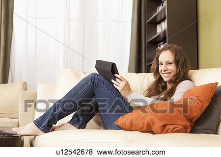 Stock Photo - Smiling woman sitting on sofa with digital tablet. Fotosearch