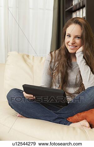 Smiling woman sitting on sofa with digital tablet View Large Photo Image Stock Photo - Smiling woman sitting on sofa with digital tablet. Fotosearch