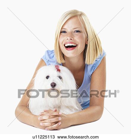 Stock Image - Studio Shot, Portrait of smiling young woman lying down with her dog. Fotosearch