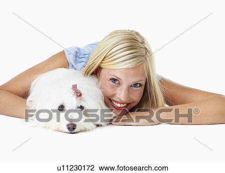 Stock Image - Studio Shot, Portrait of young woman lying down with het dog. Fotosearch