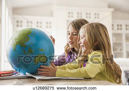 Stock Photography - Two girls (6-7) doing homework with globe. Fotosearch
