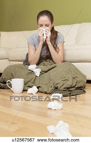 Stock Photo - Woman in living room blowing her nose. Fotosearch