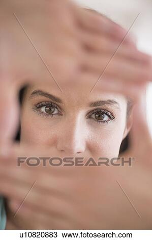 Stock Image - Woman looking at camera through handsframe. Fotosearch