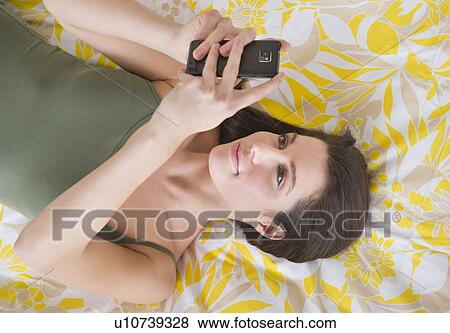 Stock Photo - Woman lying on bed and texting. Fotosearch