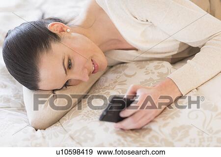 Stock Photo - Woman lying on bed and using phone. Fotosearch