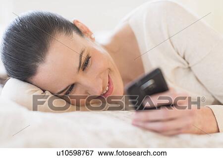 Stock Photo - Woman lying on bed and using phone. Fotosearch