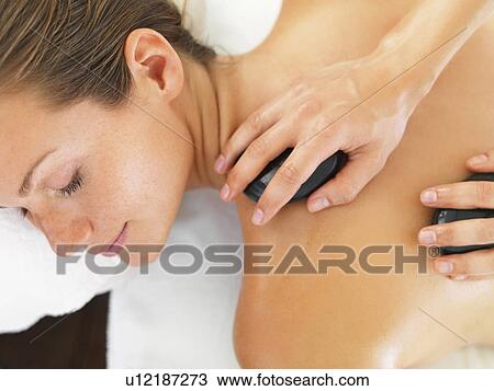 Stock Image - Woman relaxing while getting stone massage. Fotosearch