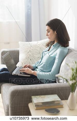 Stock Image - Woman sitting on sofa and using laptop. Fotosearch