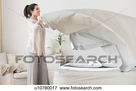 Stock Photo - Woman spreading sheet on bed. Fotosearch