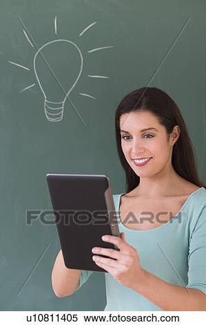 Stock Photography - Woman using digital tablet in front of blackboard. Fotosearch