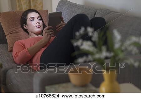 Woman using digital tablet while lying on sofa View Large Photo Image Picture - Woman using digital tablet while lying on sofa. Fotosearch