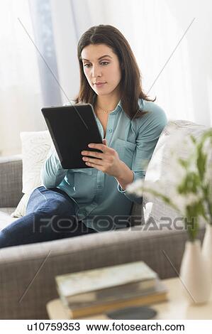 Stock Image - Woman using digital tablet while sitting on sofa. Fotosearch