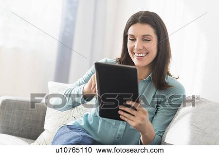 Woman using digital tablet while sitting on sofa View Large Photo Image Stock Image - Woman using digital tablet while sitting on sofa. Fotosearch