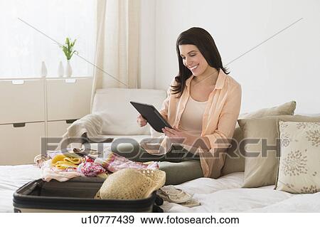 Woman using digital tablet while packing suitcase View Large Photo Image Stock Photo - Woman using digital tablet while packing suitcase. Fotosearch