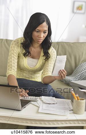 Stock Photograph - Woman using laptop and going through bills. Fotosearch