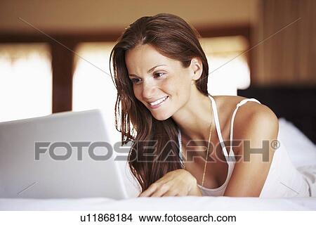 Picture - Woman using laptop while lying in bed. Fotosearch
