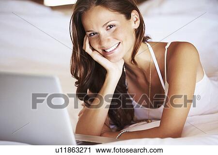 Stock Image - Woman using laptop while lying in bed. Fotosearch
