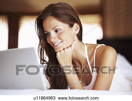 Stock Image - Woman using laptop while lying in bed. Fotosearch