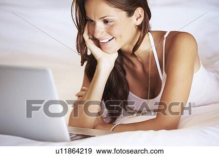 Woman using laptop while lying in bed View Large Photo Image Stock Photo - Woman using laptop while lying in bed. Fotosearch