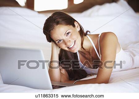 Stock Photography - Woman using laptop while lying in bed. Fotosearch