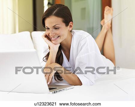 Woman using laptop while lying on bed View Large Photo Image Stock Image - Woman using laptop while lying on bed. Fotosearch