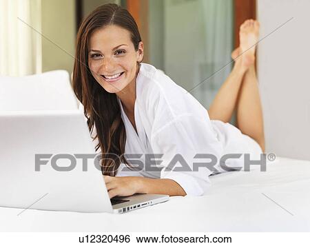 Stock Photograph - Woman using laptop while lying on bed. Fotosearch