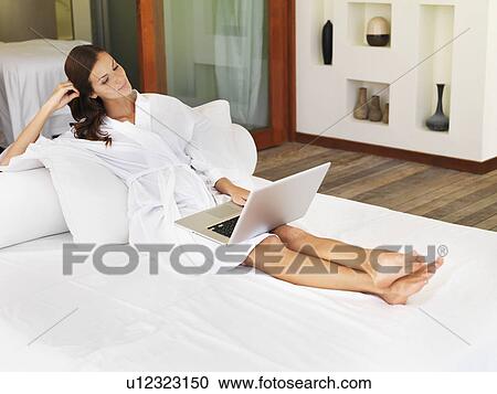 Woman using laptop while sitting on bed View Large Photo Image Stock Image - Woman using laptop while sitting on bed. Fotosearch