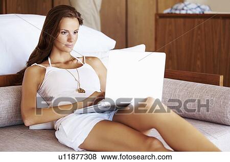 Woman using laptop while sitting on bed View Large Photo Image Stock Photo - Woman using laptop while sitting on bed. Fotosearch