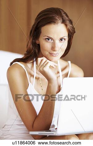 Stock Photograph - Woman using laptop while sitting on bed. Fotosearch