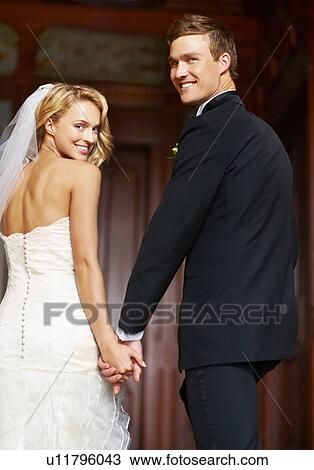 Stock Image - Young couple looking over shoulders towards camera. Fotosearch