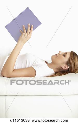 Stock Photo - Young woman lying on bed and reading. Fotosearch