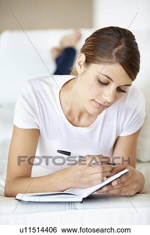 Stock Photograph - Young woman lying on bed and reading. Fotosearch