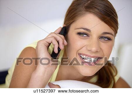 Stock Photo - Young woman lying on bed and talking on phone. Fotosearch