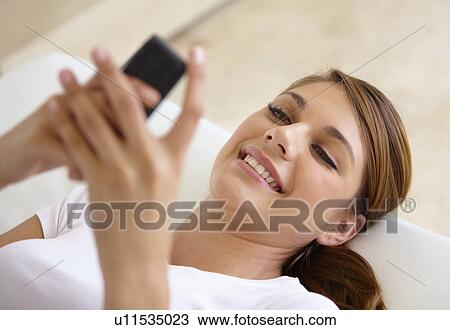 Young woman lying on bed and using cell phone View Large Photo Image Stock Image - Young woman lying on bed and using cell phone. Fotosearch