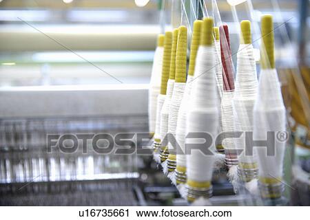 Stock Image - Bobbins of thread in loom in textile mill. Fotosearch