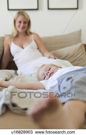 Stock Image - Boy laying on bed with mother. Fotosearch