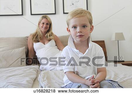 Stock Photo - Boy sitting on bed with mother. Fotosearch