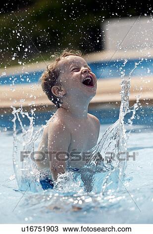 Stock Image - Boy splashing in swimming pool. Fotosearch