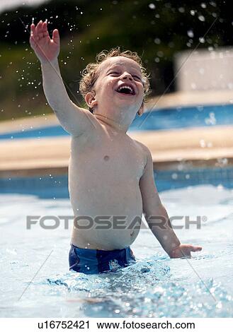 Stock Image - Boy splashing in swimming pool. Fotosearch