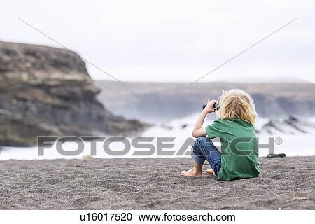 Stock Image - Boy using binoculars on beach. Fotosearch