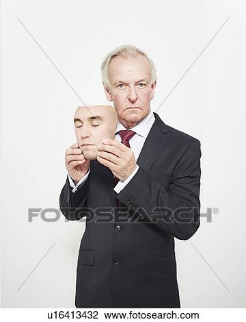 Stock Image - Businessman holding mask. Fotosearch