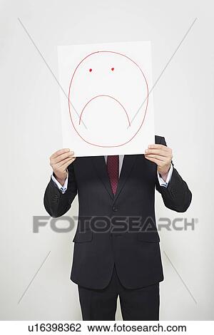 Stock Image - Businessman holding sad face over his face. Fotosearch