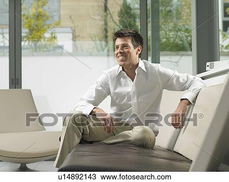 Stock Image - Businessman on sofa in office lobby. Fotosearch