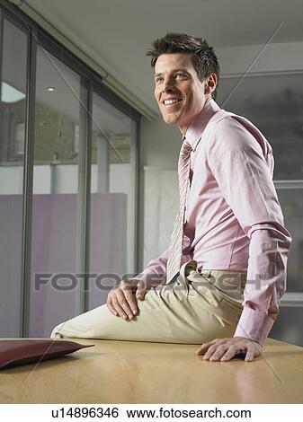 Stock Photograph - Businessman sitting on desk. Fotosearch