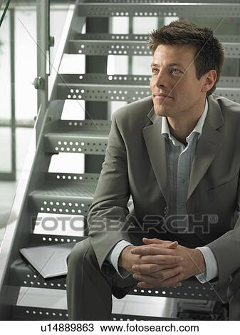Stock Image - Businessman sitting on steps in office. Fotosearch