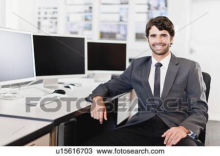 Stock Image - Businessman smiling at desk. Fotosearch