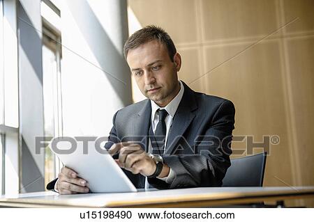 Stock Image - Businessman using tablet computer at desk. Fotosearch